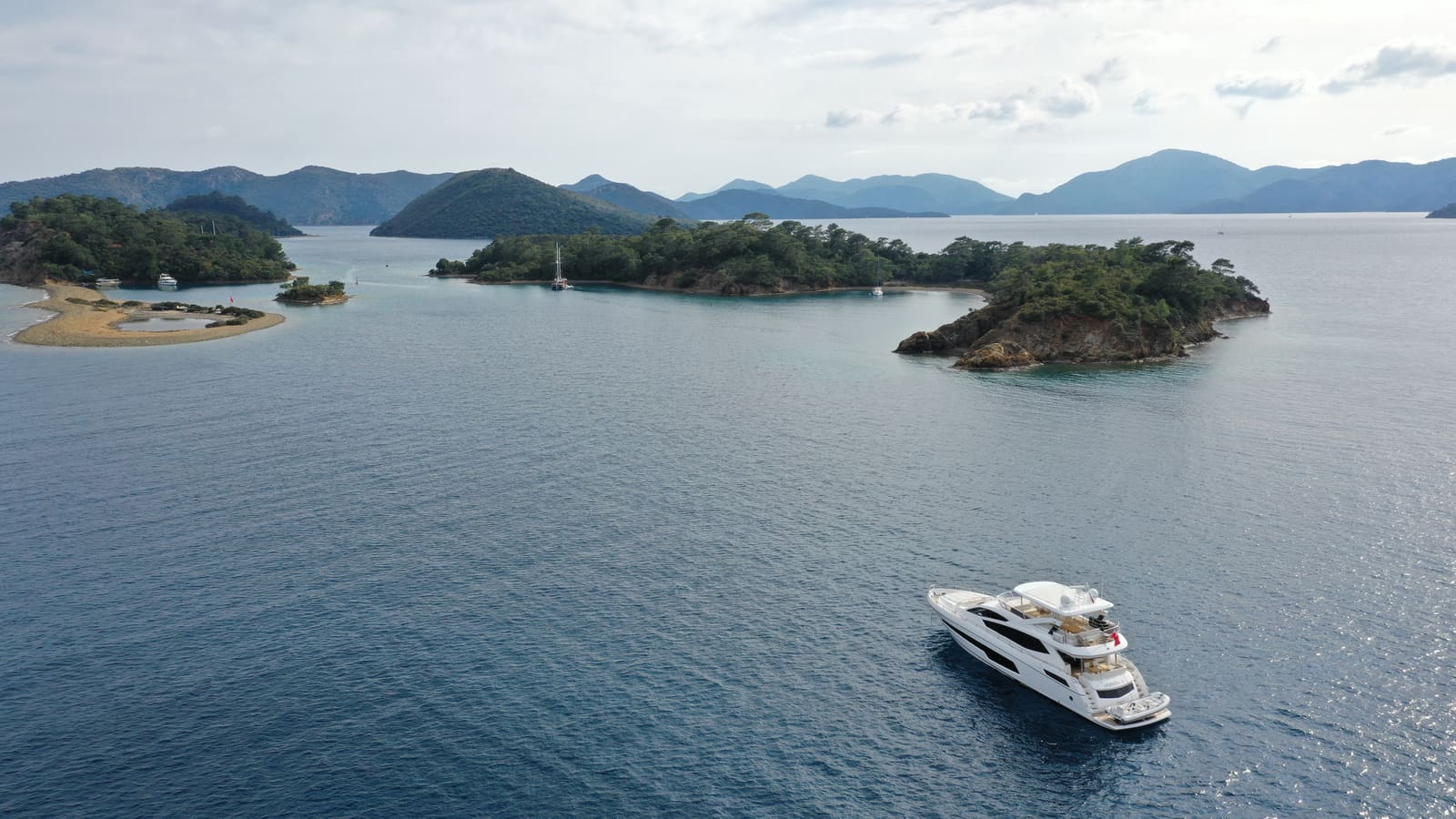 The pine-covered islands of Göcek from the air, with a motor yacht at anchor in the foreground